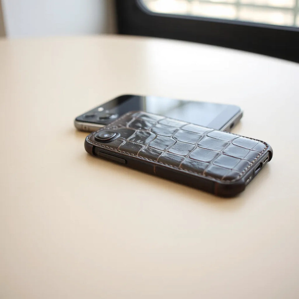 Textured crocodile leather phone case with subtle sheen on a light tabletop under soft window light