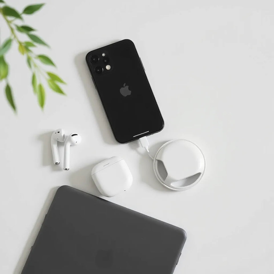 Minimal desk setup with an iPhone, wireless earbuds, charging cable, charging puck, and slim protective case.